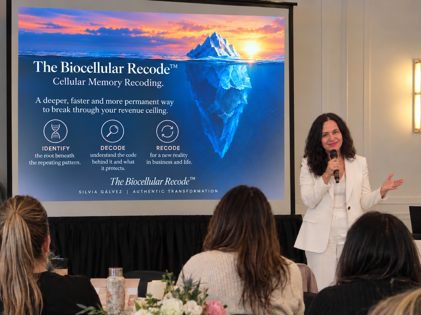 Silvia Gálvez speaking on stage explaining Cellular Memory Recoding, identifying, decoding, and recoding revenue ceilings on a presentation screen.